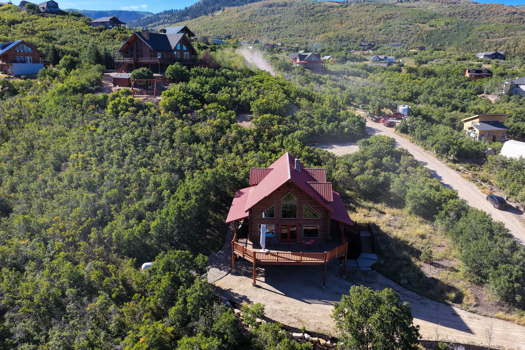 Wood-sided exterior featuring a red-pitched roof, expansive deck, and a surrounding natural landscape