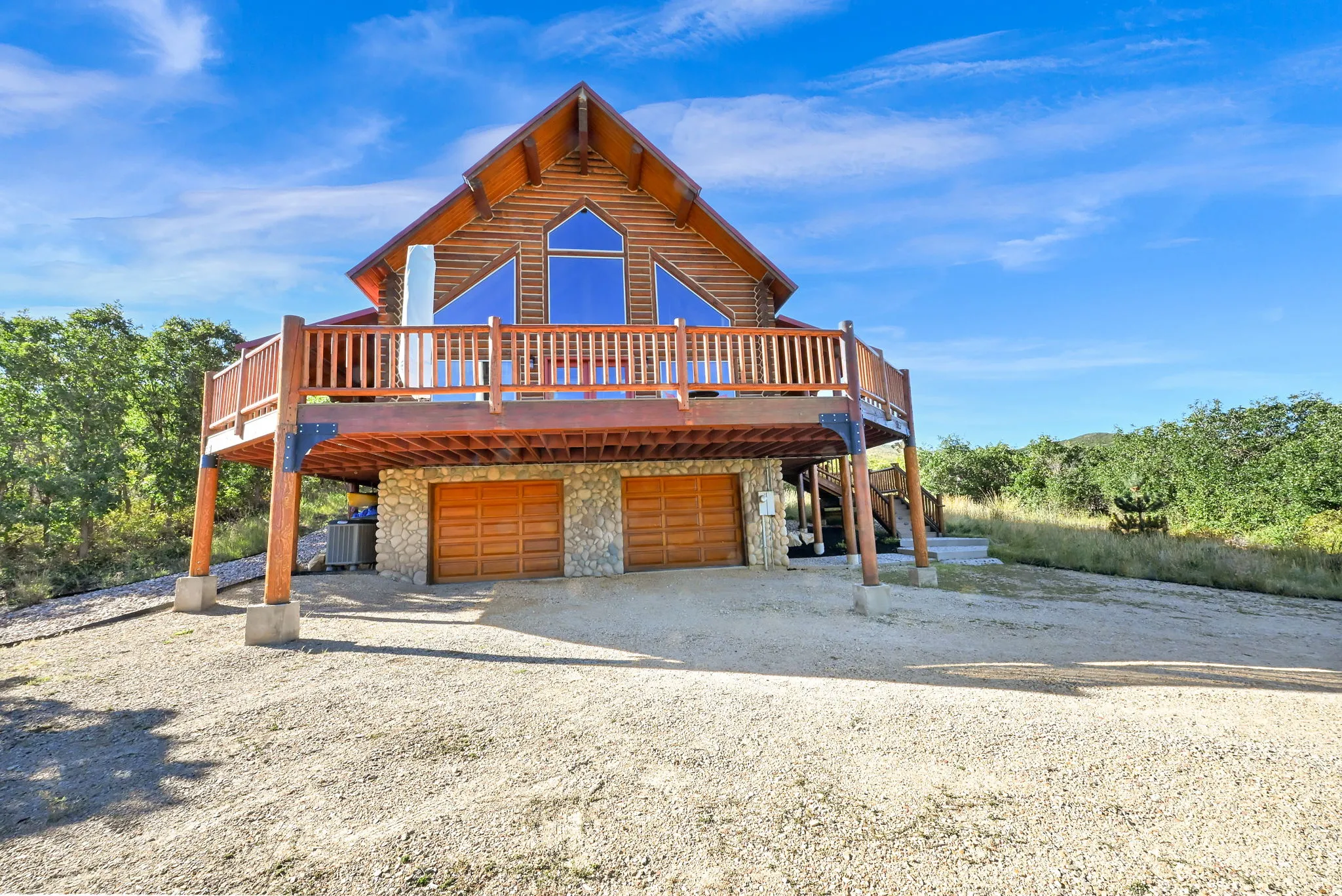 Wood-sided exterior with expansive upper deck, stone-faced ground level, large pane windows, and attached garage with wood-finish doors