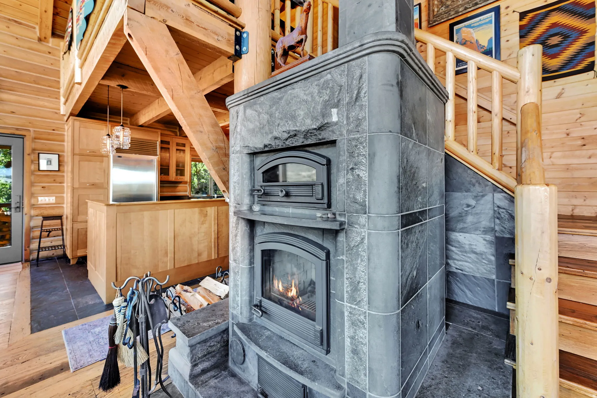 Stacked stone fireplace with two fireboxes, exposed wood beam ceiling, wood plank walls, and wood staircase with log railing