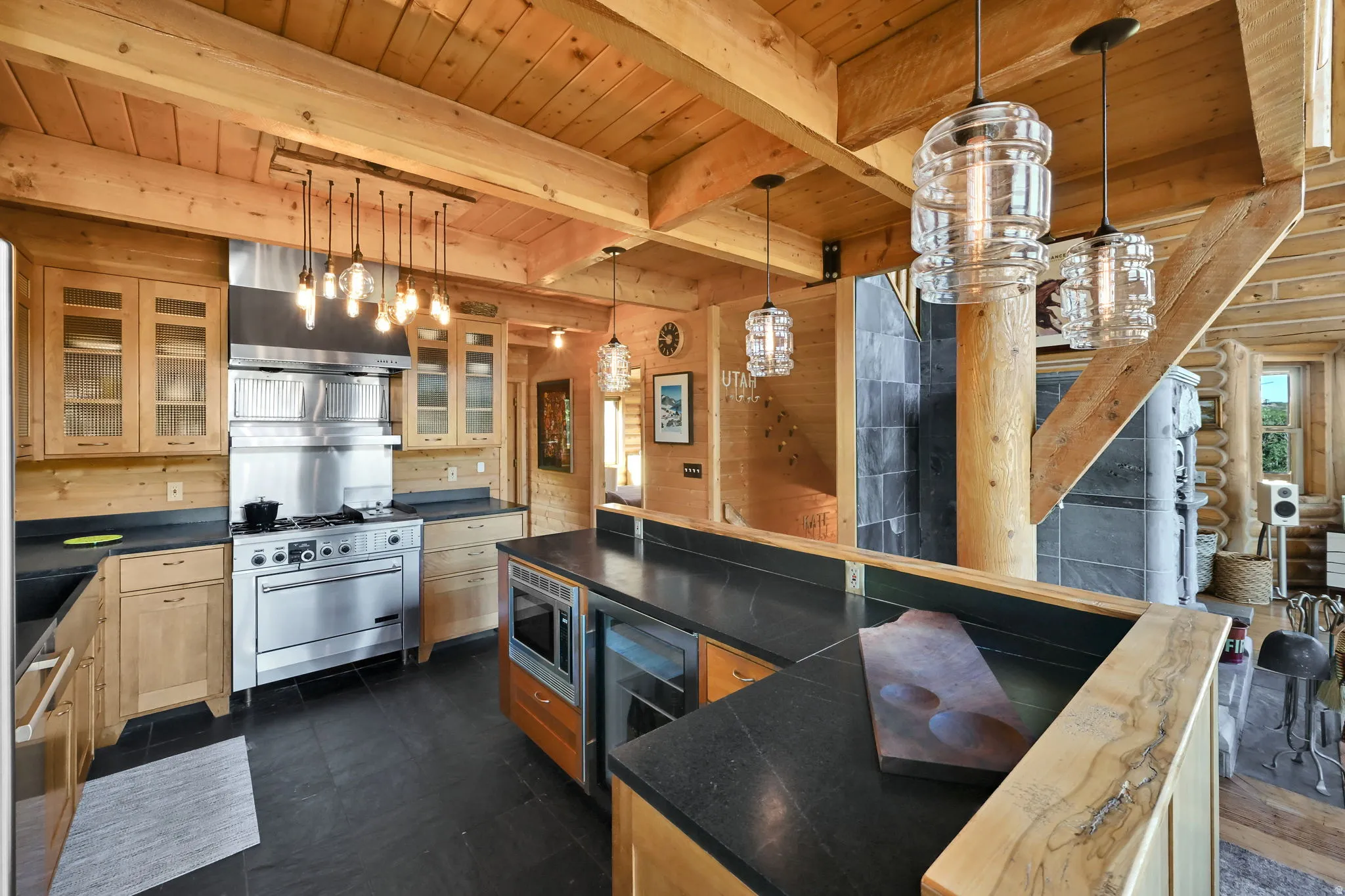 Kitchen featuring wood cabinetry with glass-front uppers, stainless steel range with hood, dark countertops, and wood-paneled ceilings with exposed beams