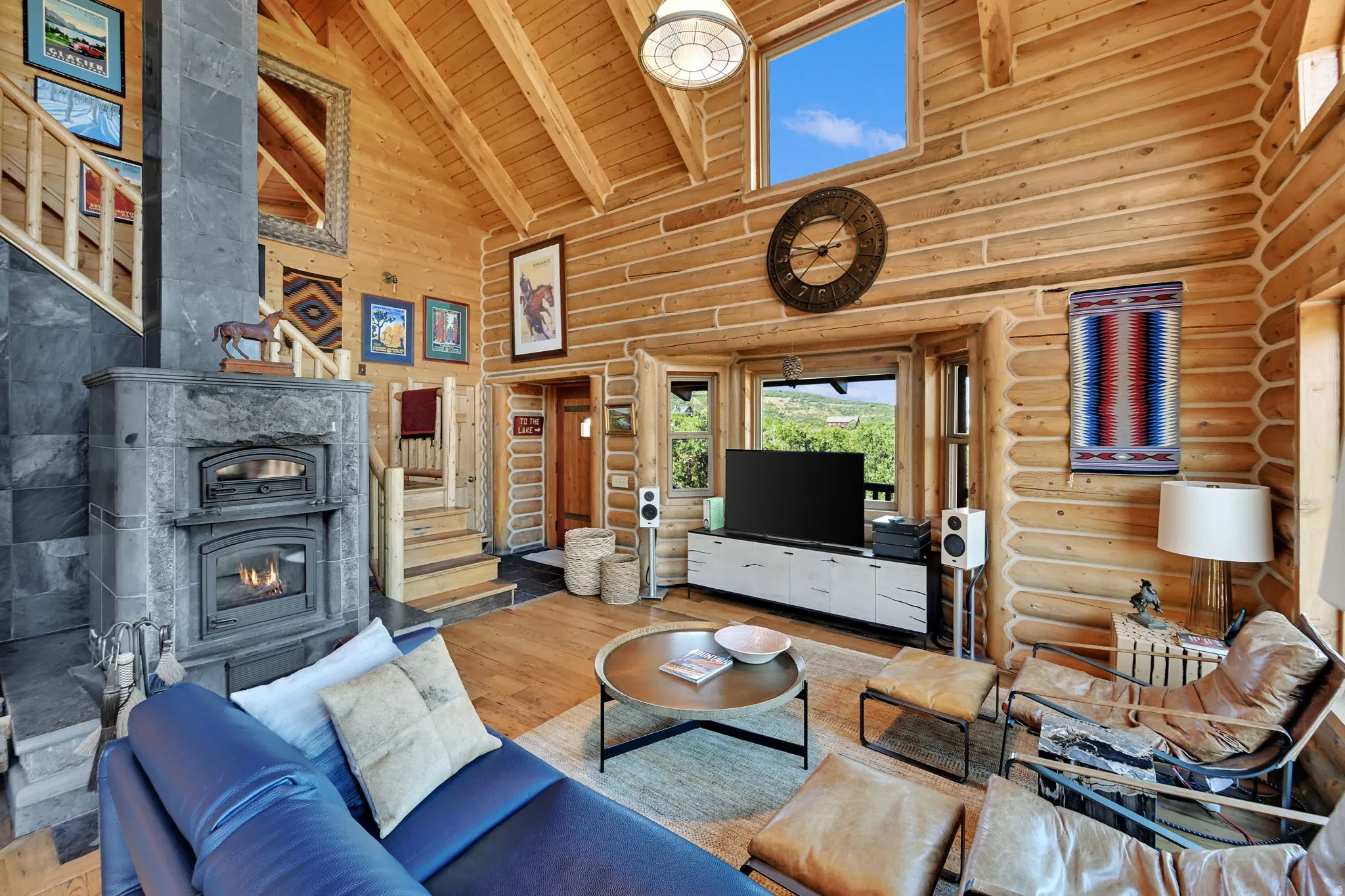Vaulted wood-plank ceilings, log wall construction, stone-clad fireplace, wood-finish flooring, and a large picture window