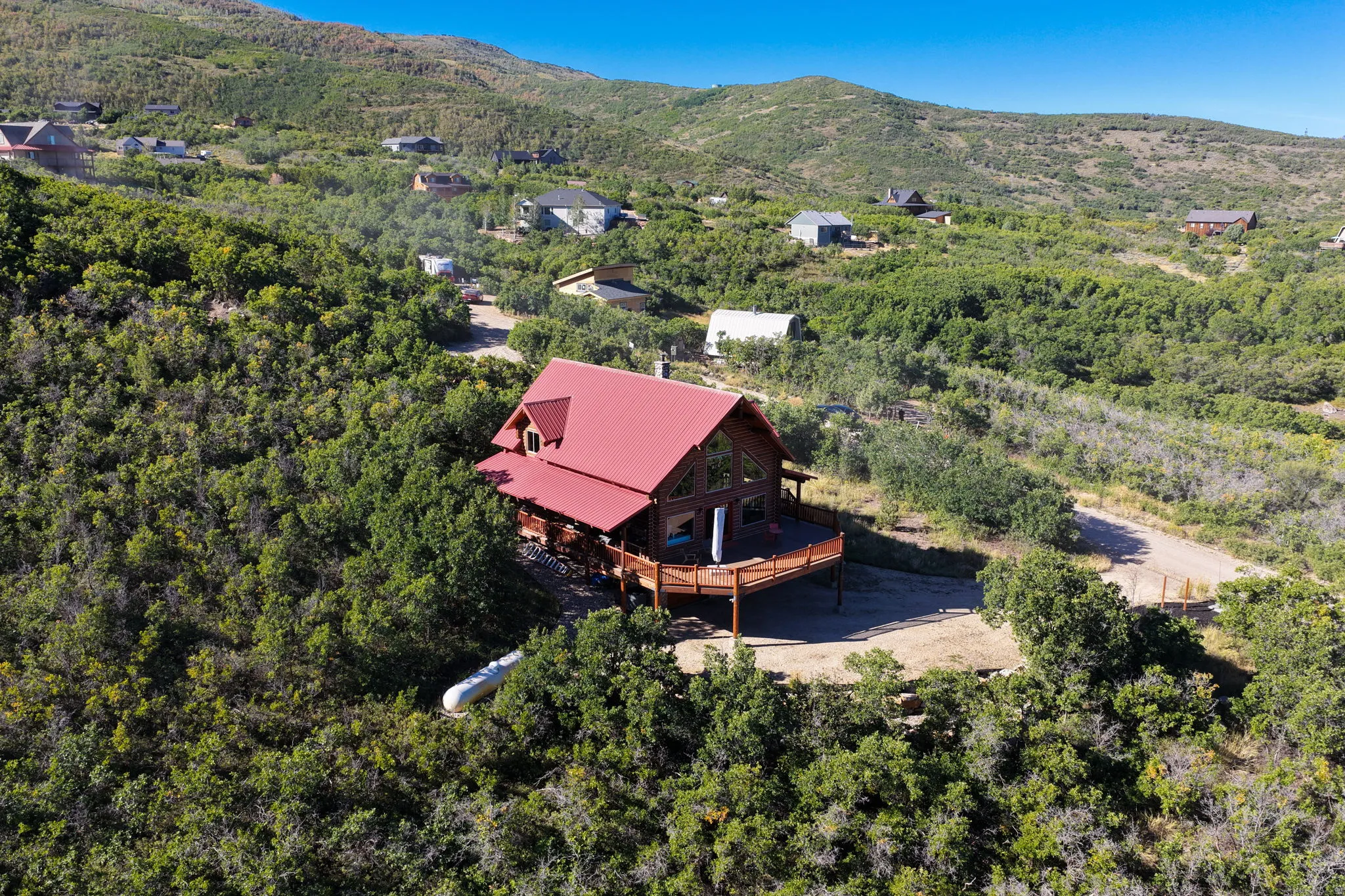 Log cabin exterior with a red roof, expansive wood deck, and surrounding natural foliage