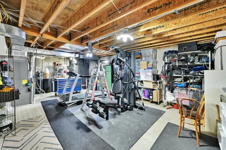 Unfinished basement featuring exposed wood joists, concrete walls, ductwork, and overhead lighting