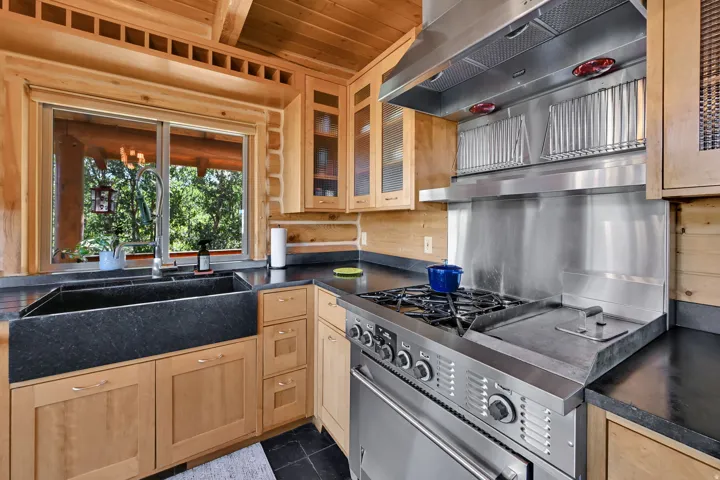 Wood plank walls and ceiling, stainless steel professional-grade range with griddle, stainless steel range hood, black farmhouse sink, and light wood cabinetry