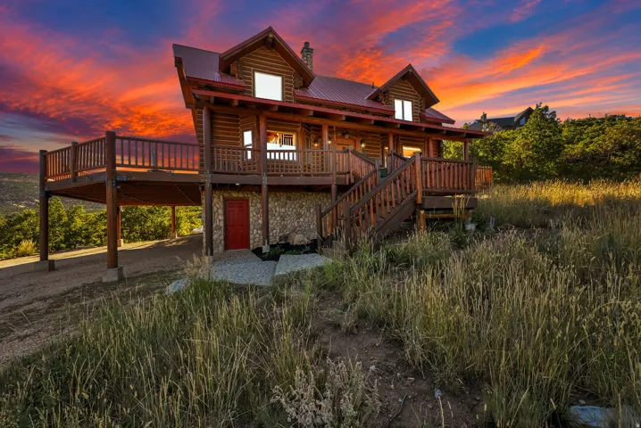 Log-sided exterior with a red metal roof, elevated wooden deck, stone foundation, and a prominent wooden staircase