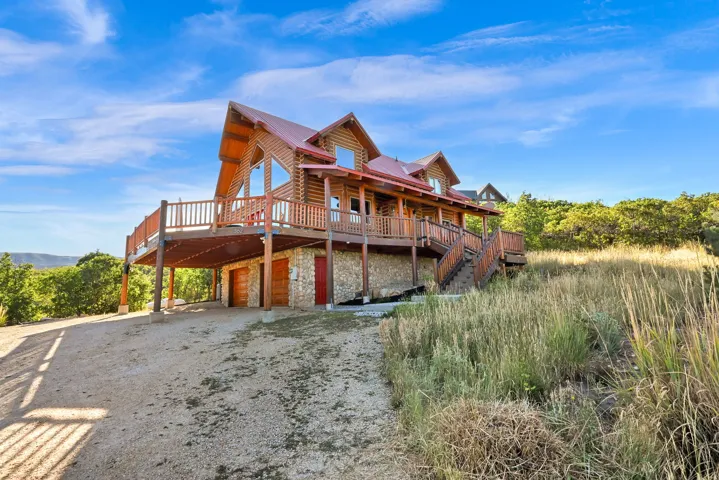 Log home exterior with a red metal roof, expansive wraparound deck with wooden railings, and a stone foundation