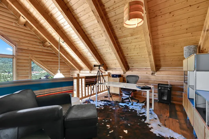 Angled wood-paneled ceilings with exposed beams, wood-finish flooring, and built-in shelving