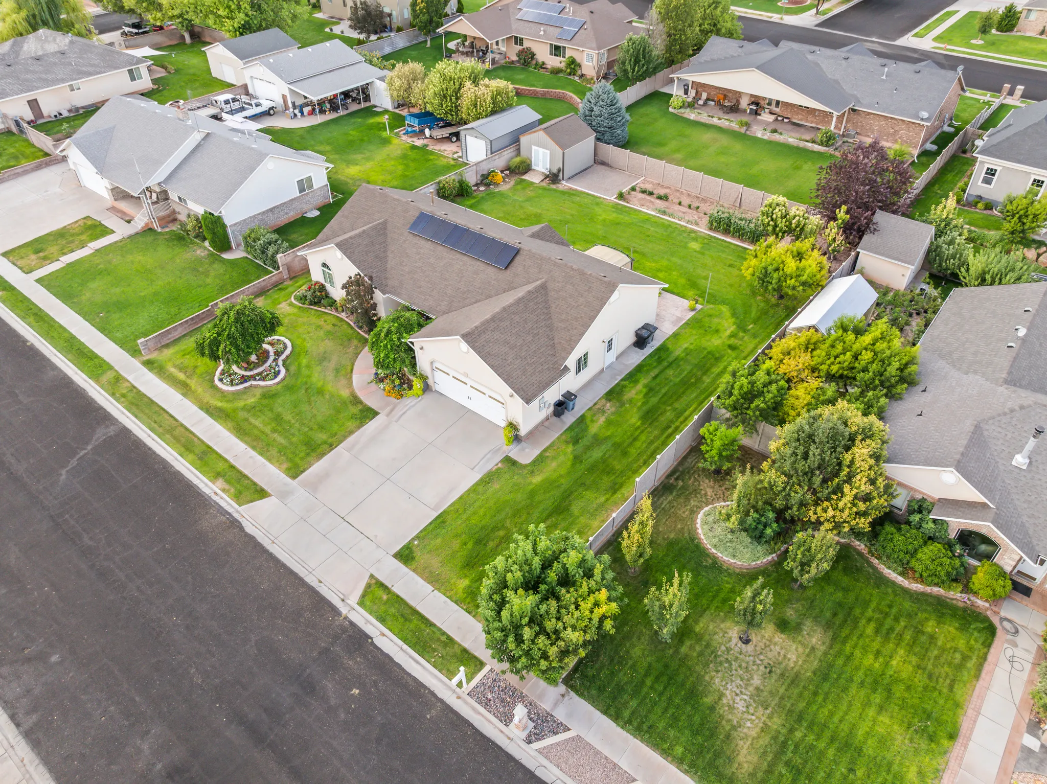 Expansive corner lot featuring a stucco exterior, attached garage, solar panels, and mature landscaping