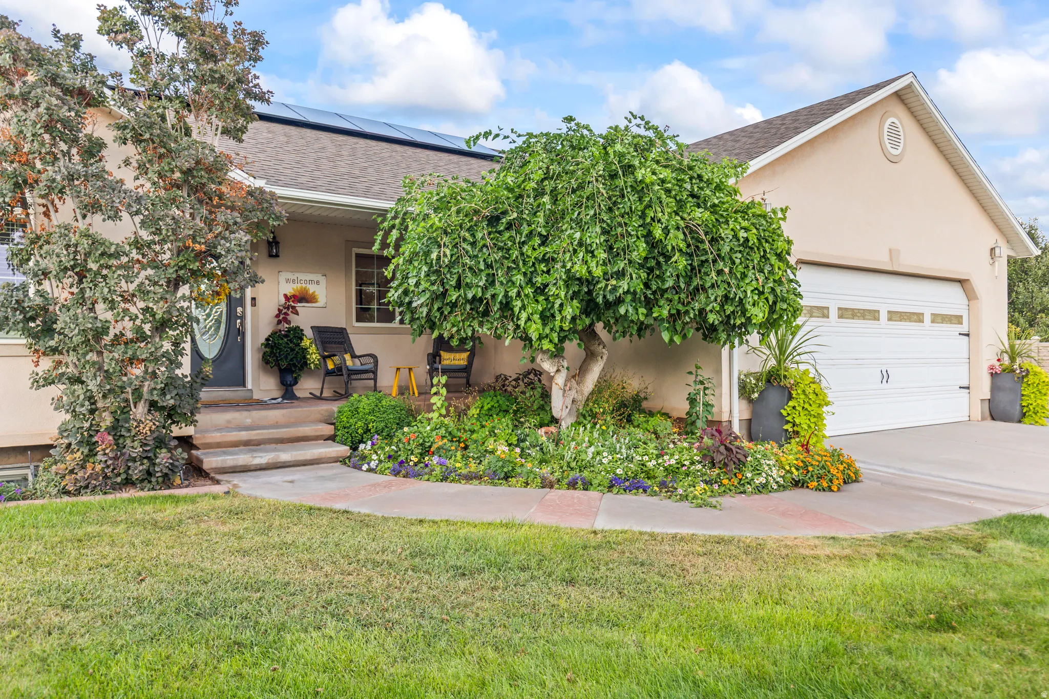 Stucco exterior with a two-car garage, mature landscaping, and solar panels