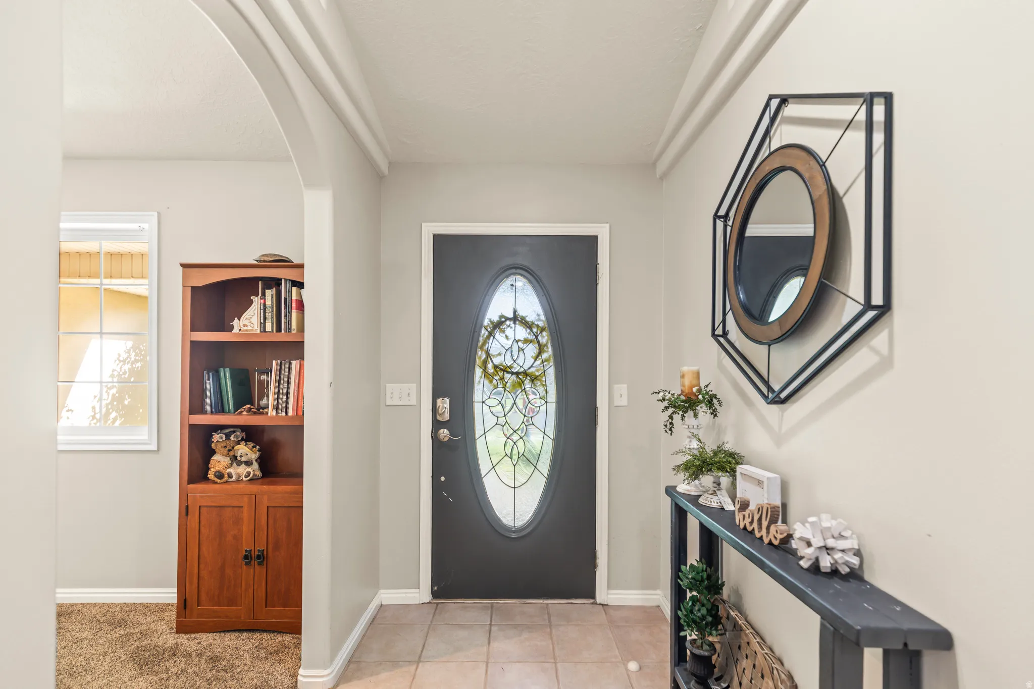 Oval-lite entry door, tile flooring, arched doorway, window, and neutral wall tones