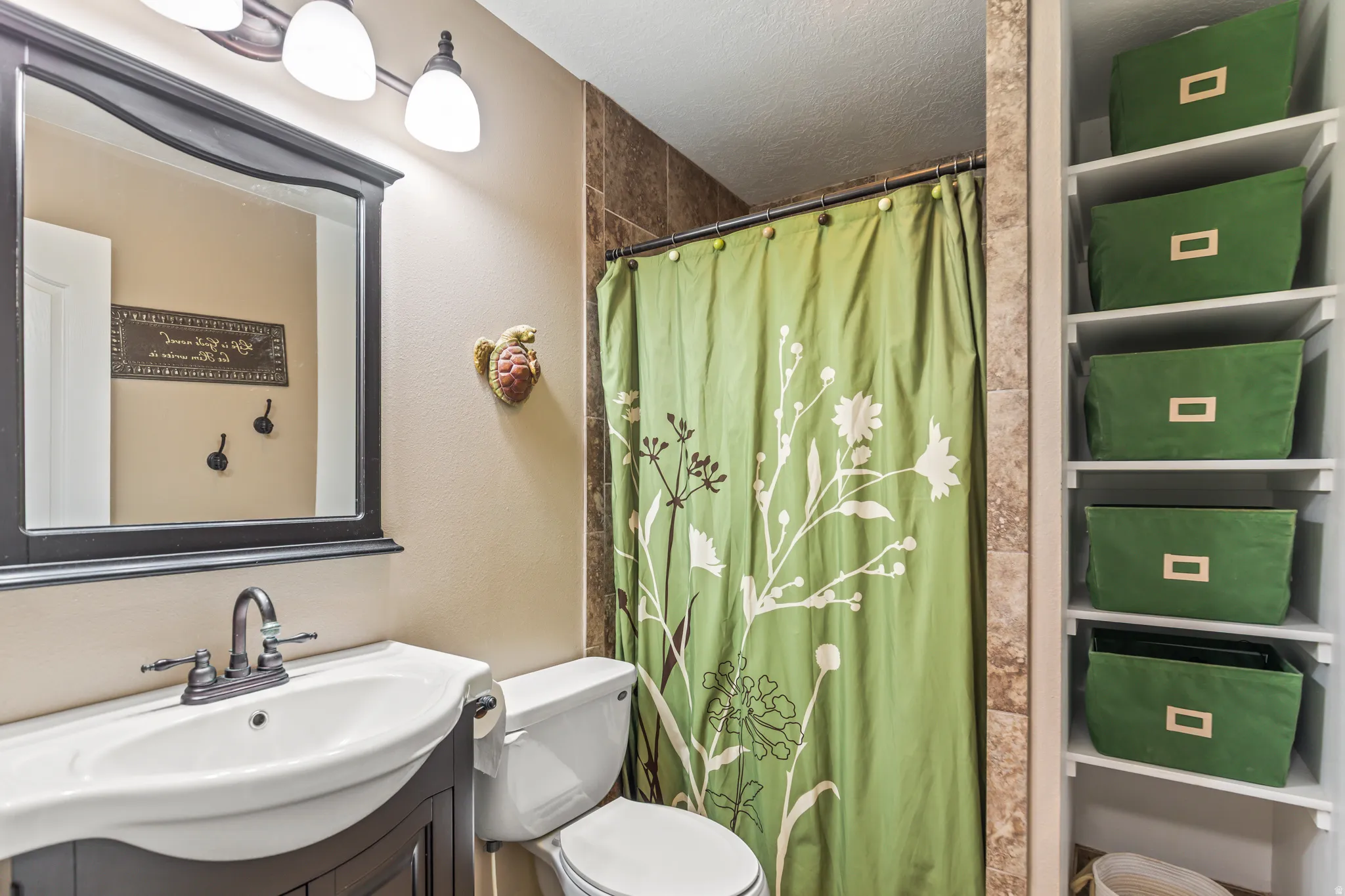 Built-in shelving, dark wood-finish vanity with integrated sink, wall-mounted light fixture, framed mirror, and tiled shower surround