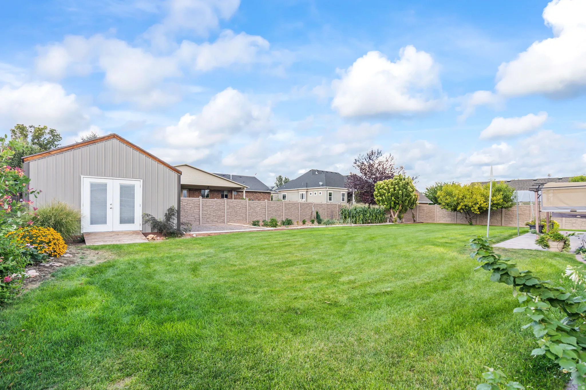 Expansive lawn area with a detached storage shed, mature trees, and a brick-finish fence