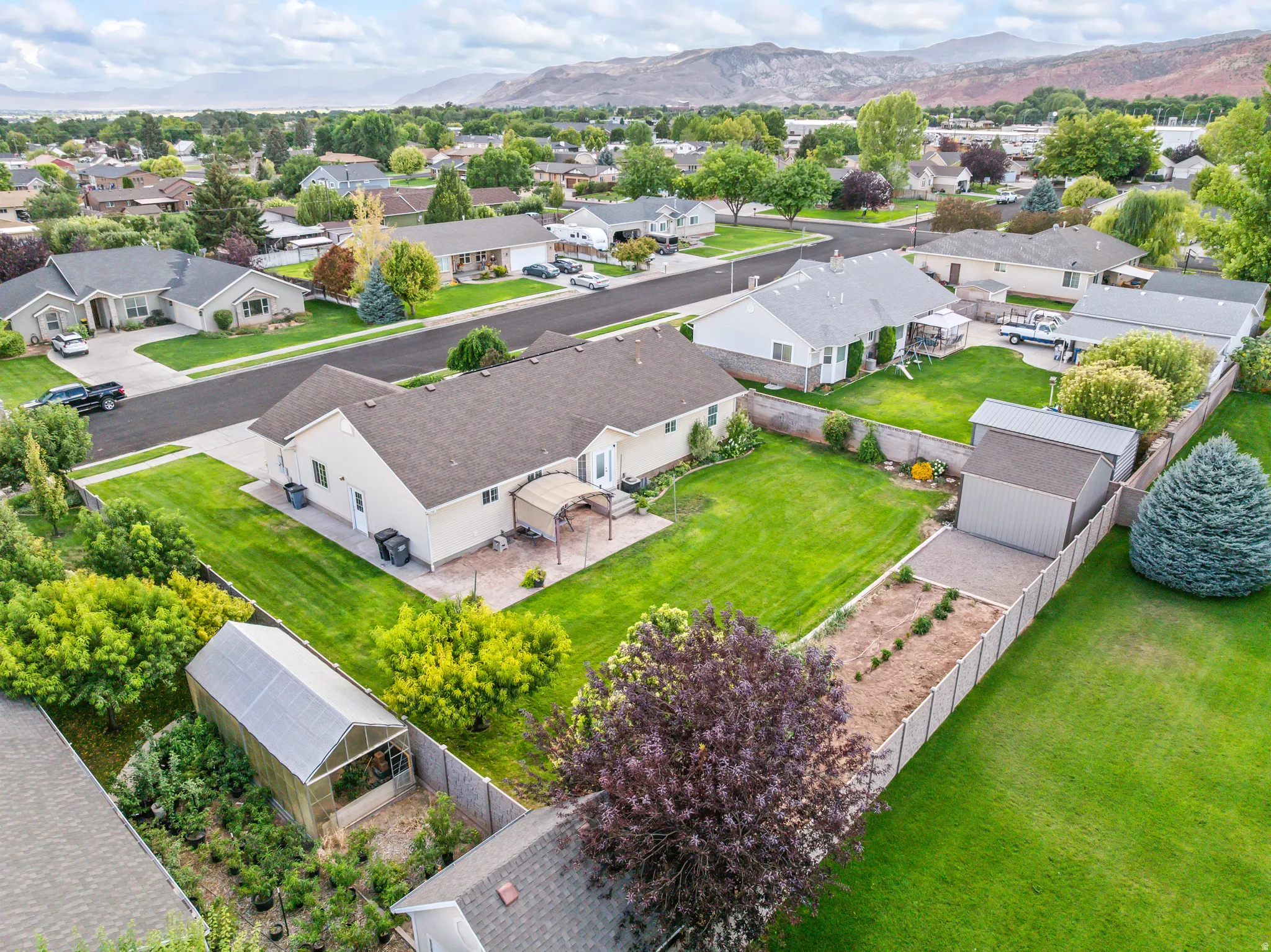 Expansive backyard featuring a manicured lawn, established landscaping, a detached shed, a greenhouse, and a paved patio with a pergola