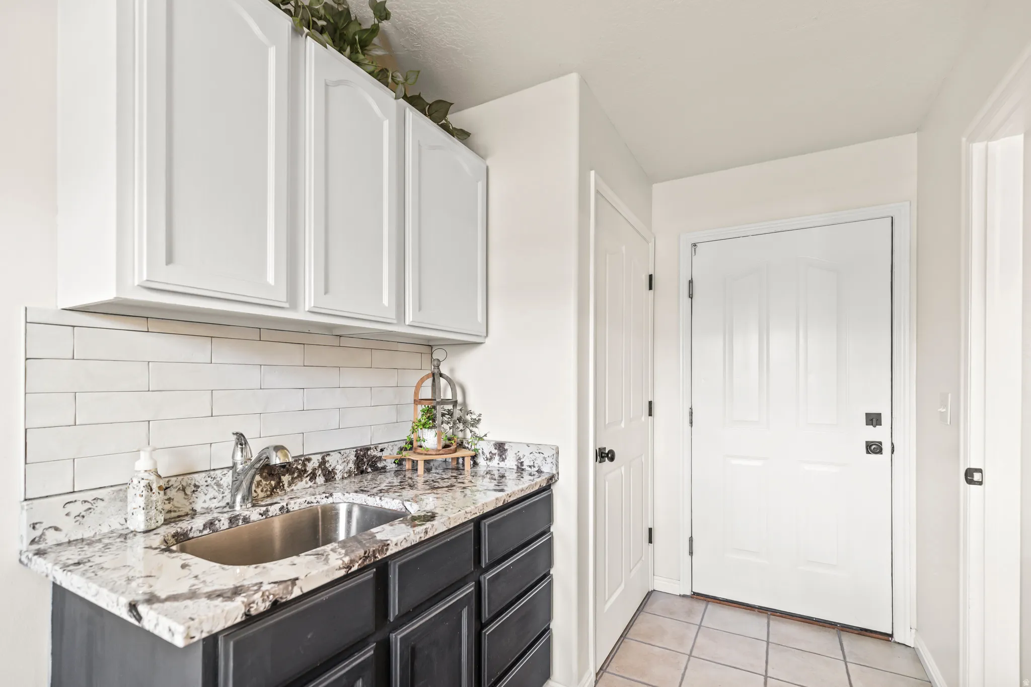 White shaker-style upper cabinetry, dark base cabinetry, light-toned granite-style countertop, stainless steel undermount sink, and white subway tile backsplash