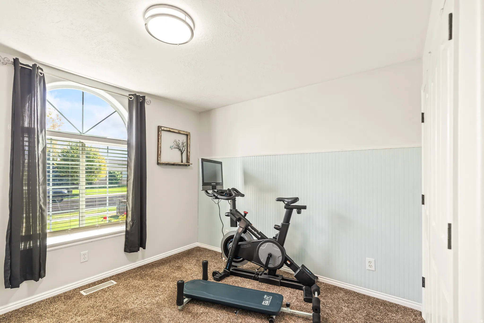 Arched window with blinds, recessed ceiling light, and vertical paneling on lower walls