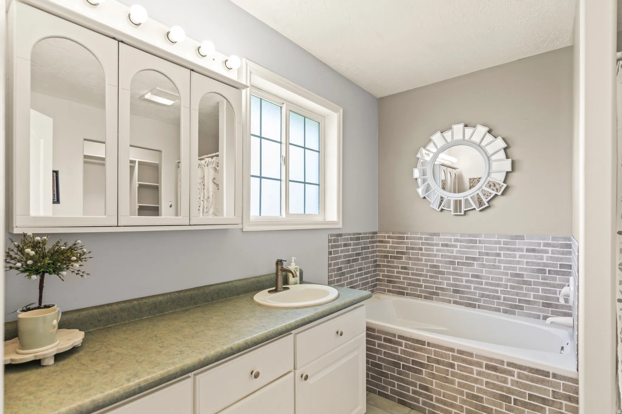 Single basin vanity with built-in cabinetry, large window with grid pattern, and a built-in bathtub with subway tile surround