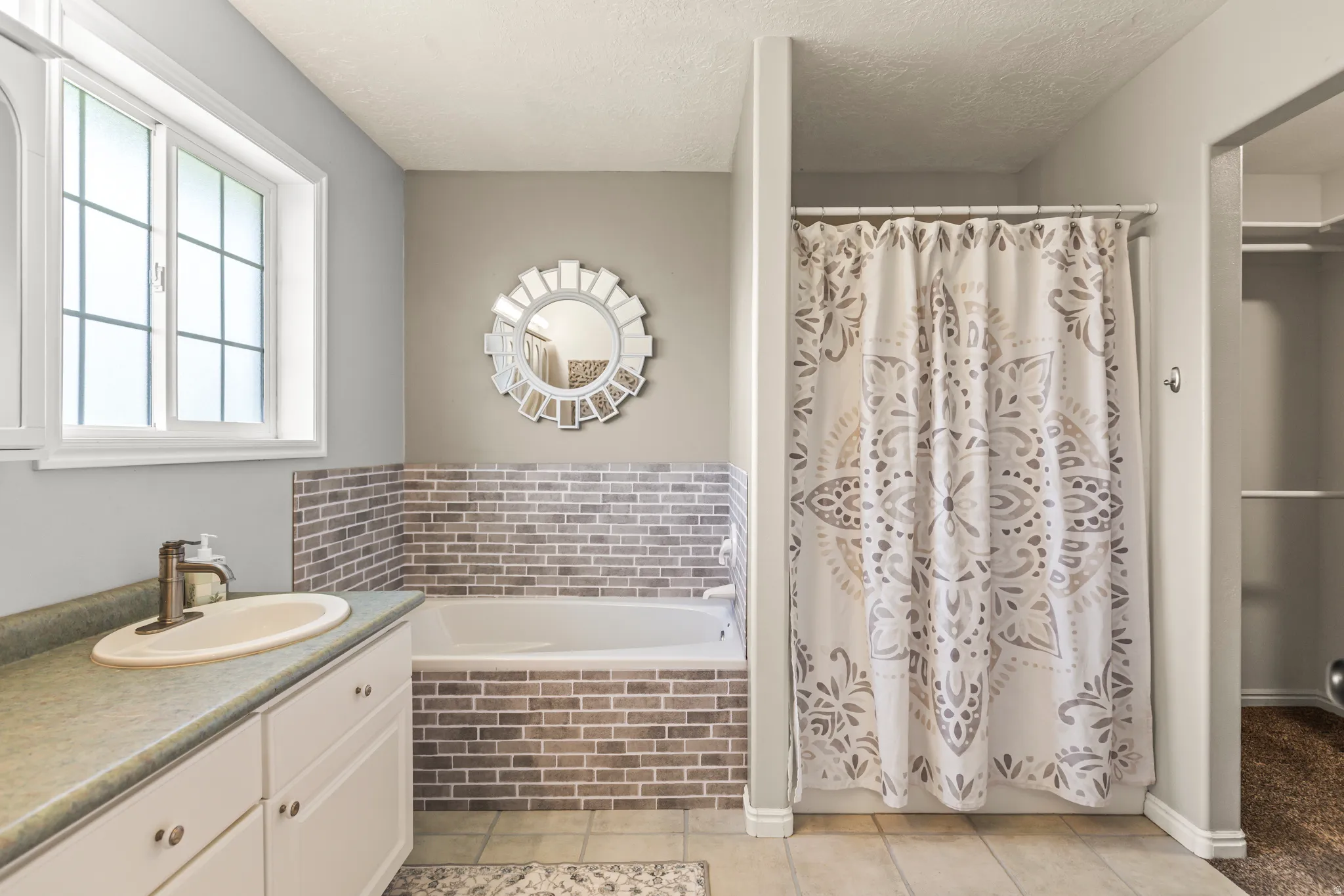 White window with grid accents, integrated bathtub with subway tile surround, white vanity with countertop, and tile flooring