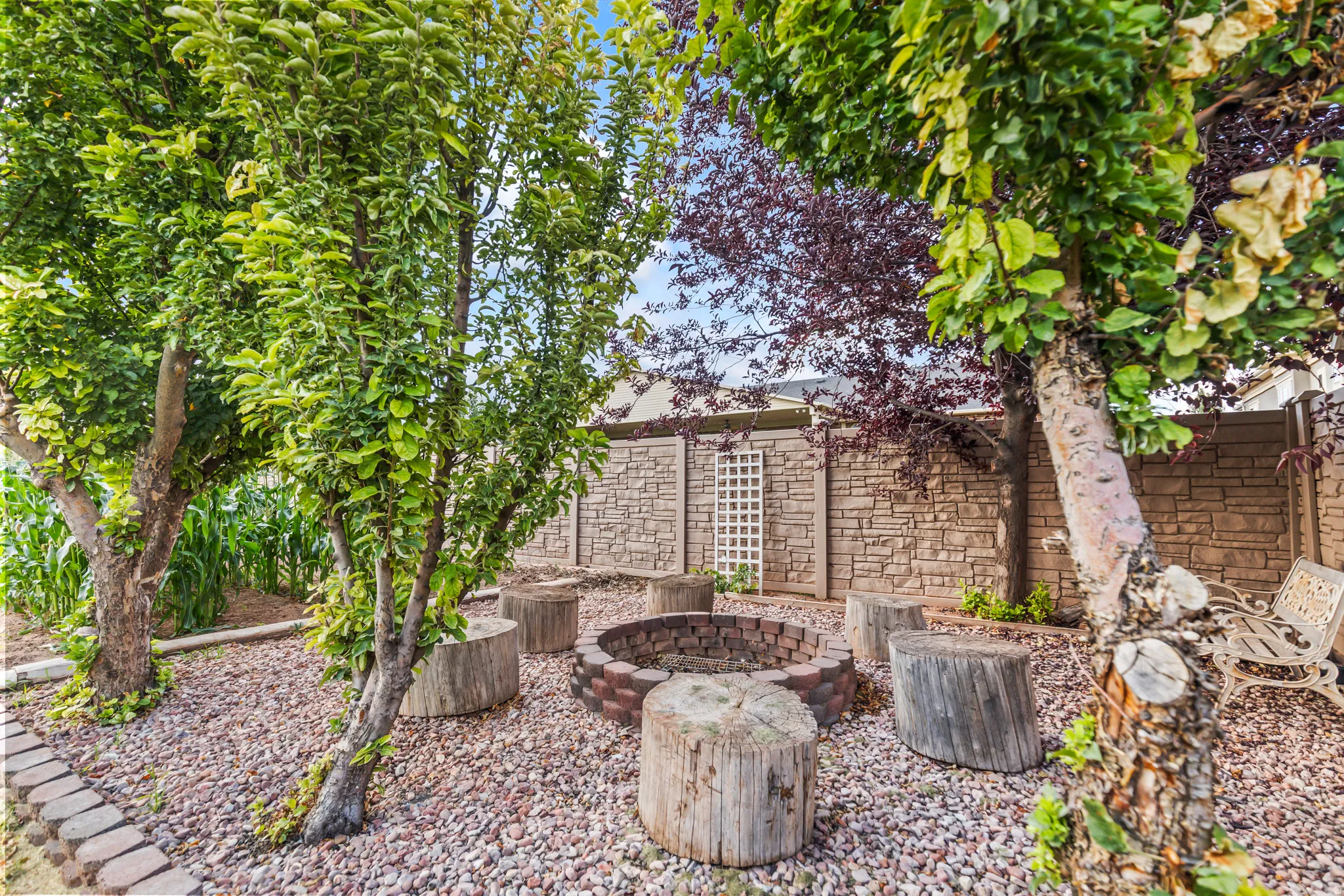 Private backyard featuring a stone fire pit, wood stump seating, mature trees, and a stone-patterned fence