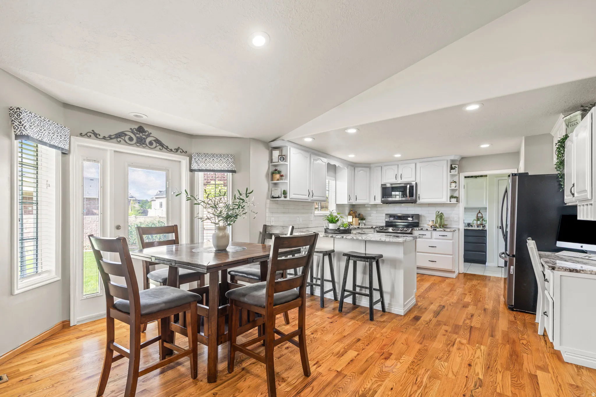 Bright kitchen and dining area featuring wood-finish flooring, white cabinetry, a built-in kitchen island, and a glass-paneled door