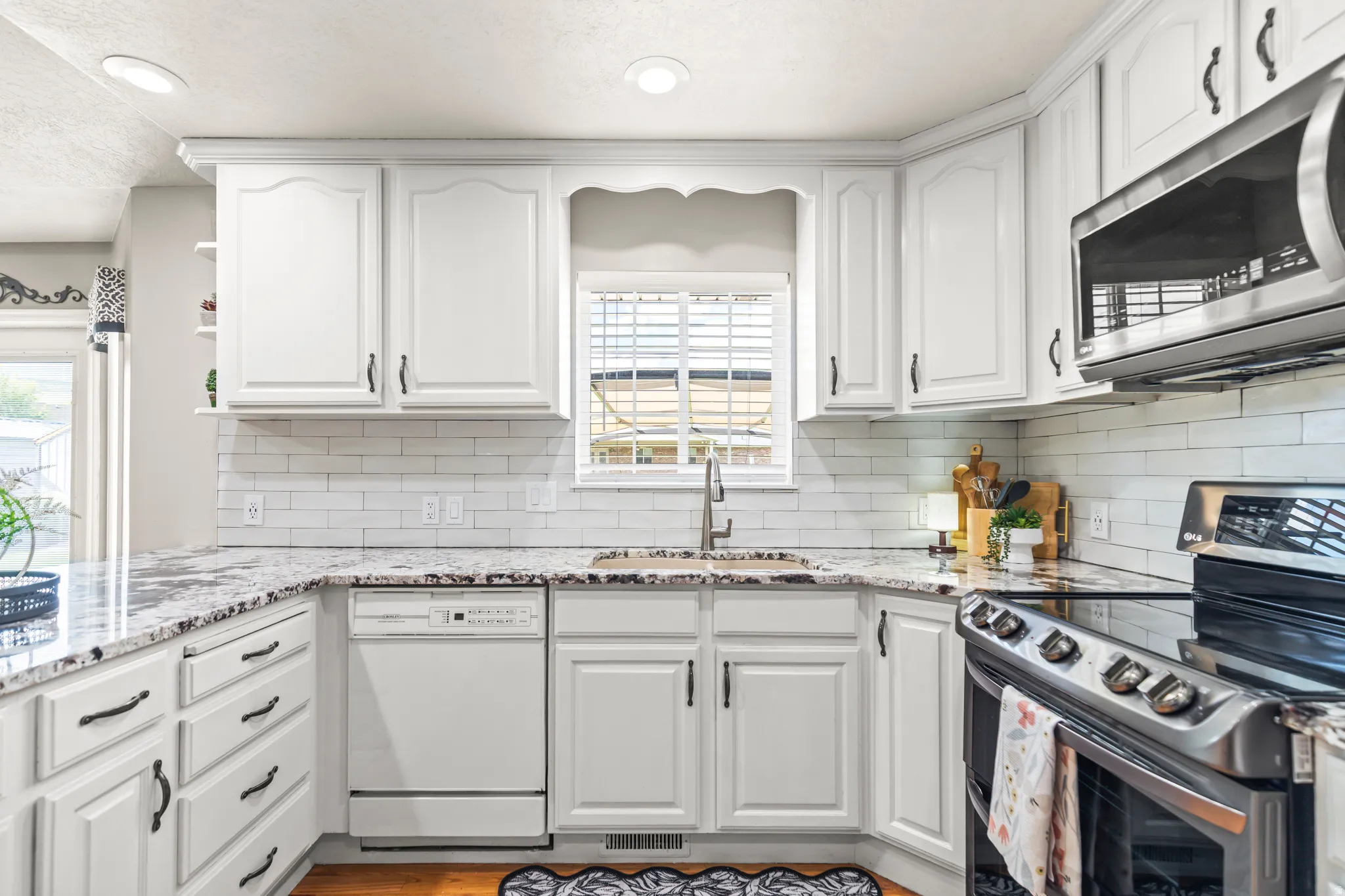 White cabinetry with dark hardware, granite-style countertops, subway tile backsplash, and stainless steel appliances