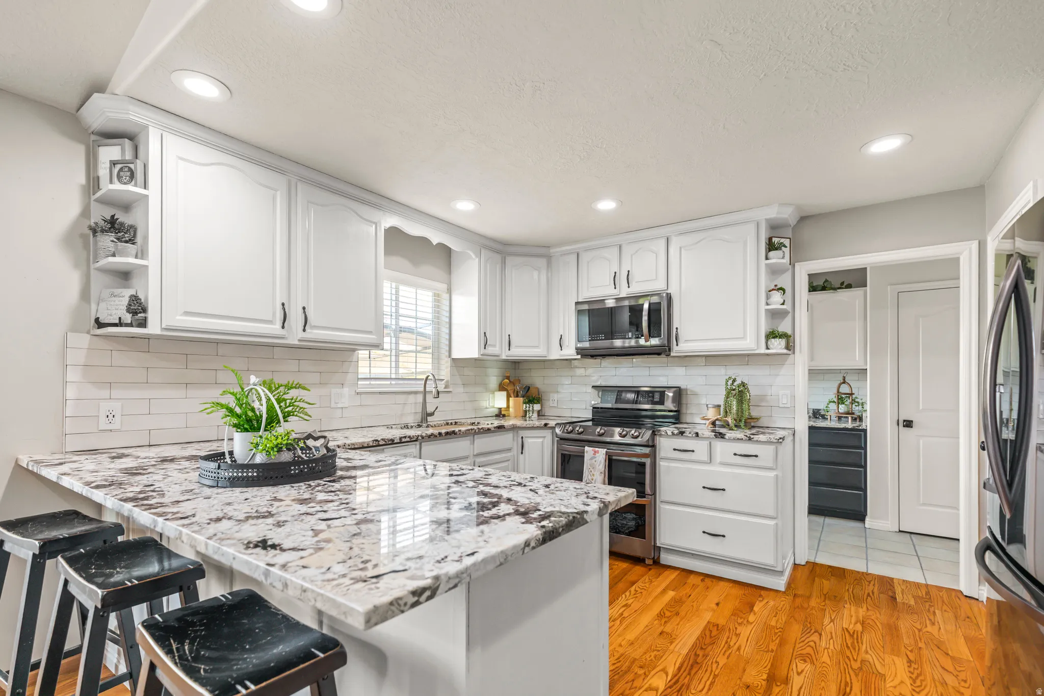 Kitchen featuring white cabinetry, a large kitchen island with a stone countertop, a subway tile backsplash, and wood-finish flooring