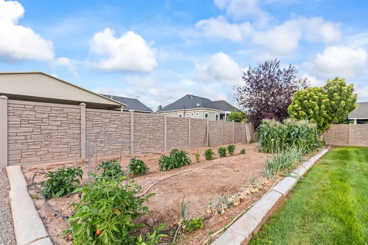 Expansive garden area featuring planted rows, concrete curbing, and a stone-look fence