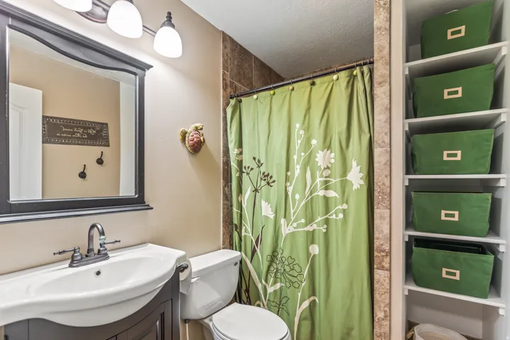 Built-in shelving, dark wood-finish vanity with integrated sink, wall-mounted light fixture, framed mirror, and tiled shower surround