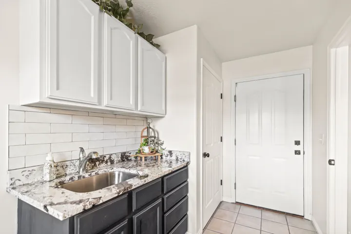 White shaker-style upper cabinetry, dark base cabinetry, light-toned granite-style countertop, stainless steel undermount sink, and white subway tile backsplash