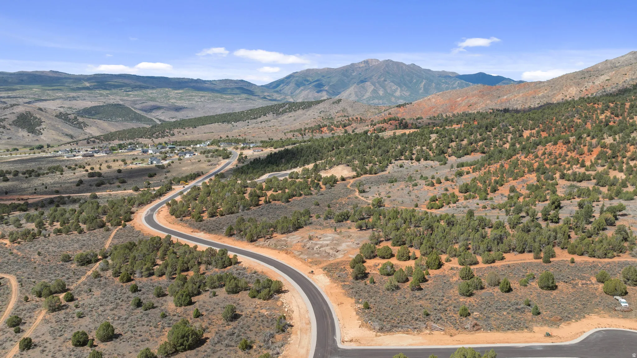 Winding paved road, surrounded by natural desert landscaping and distant mountain ranges