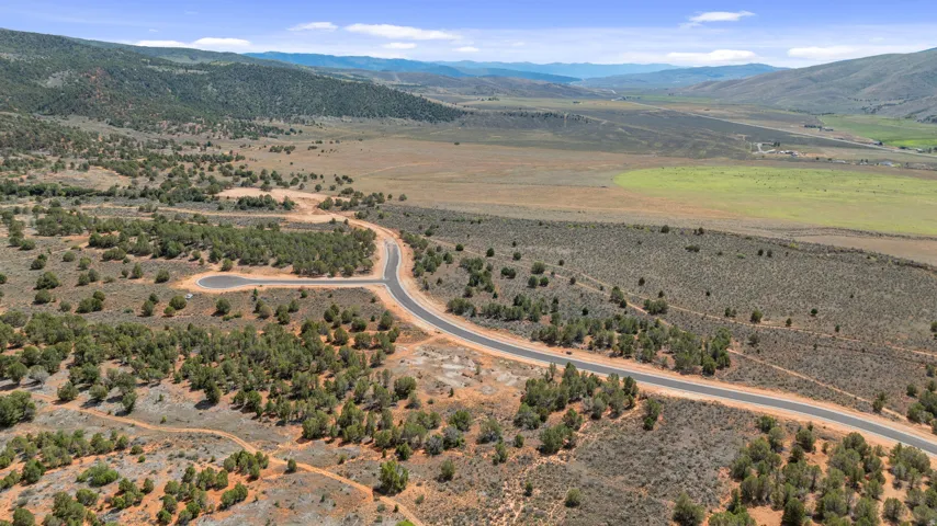 Expansive undeveloped land featuring a paved road, natural vegetation, and distant mountain scenery