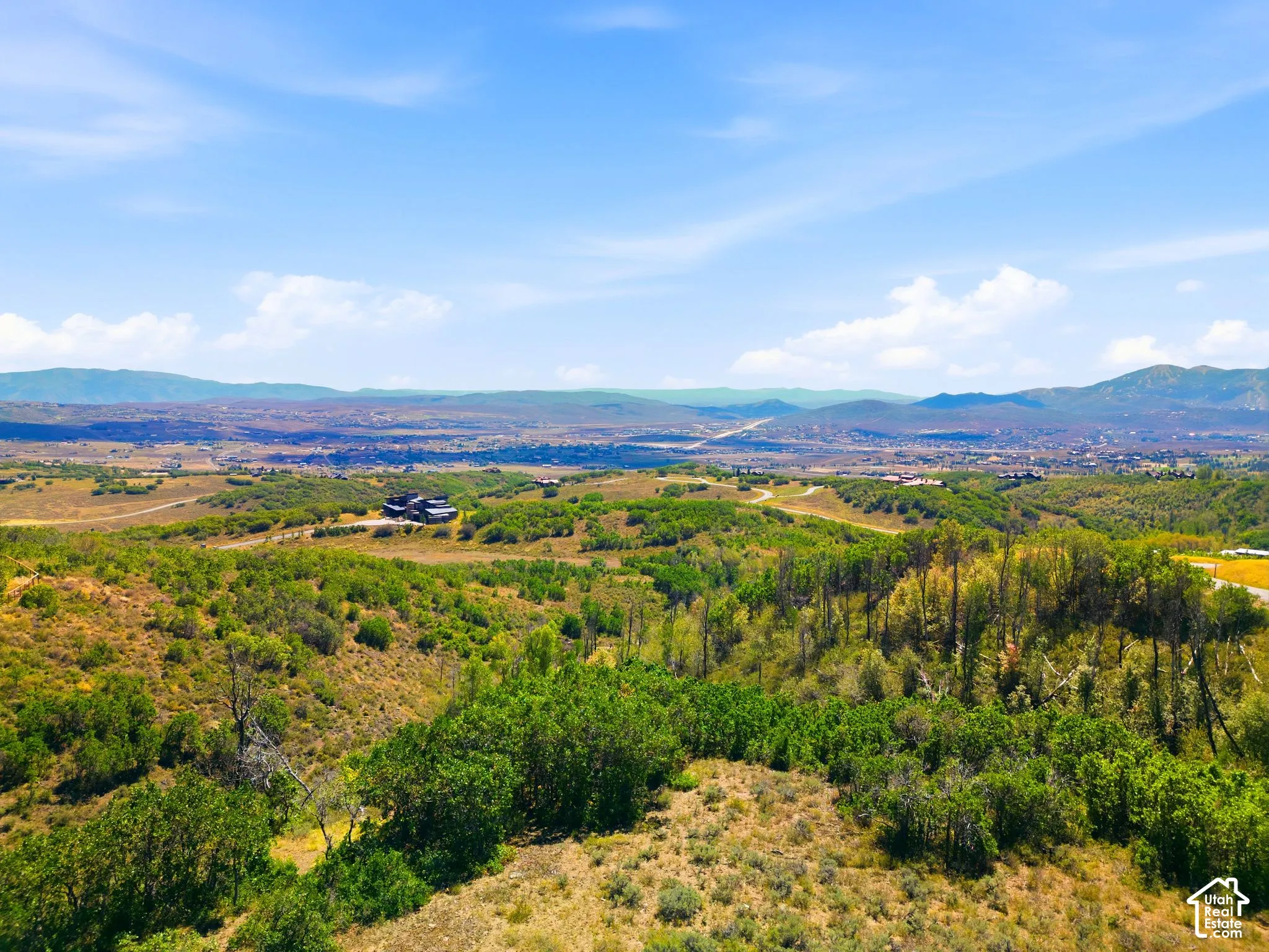 Expansive rural landscape with distant mountainous terrain, a clear blue sky, and scattered residences