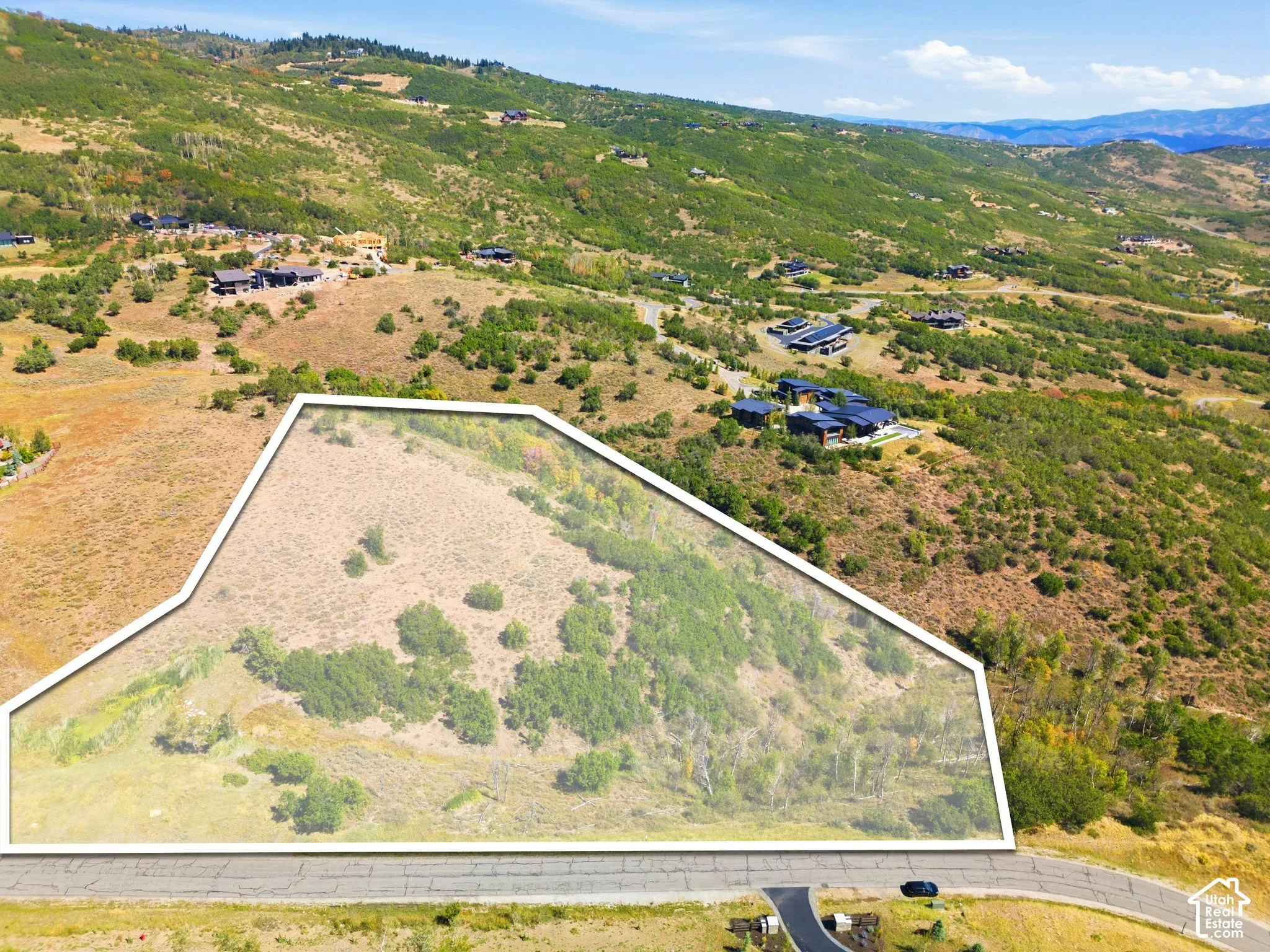 Expansive land parcel featuring natural topography, surrounding residences, and a paved road frontage
