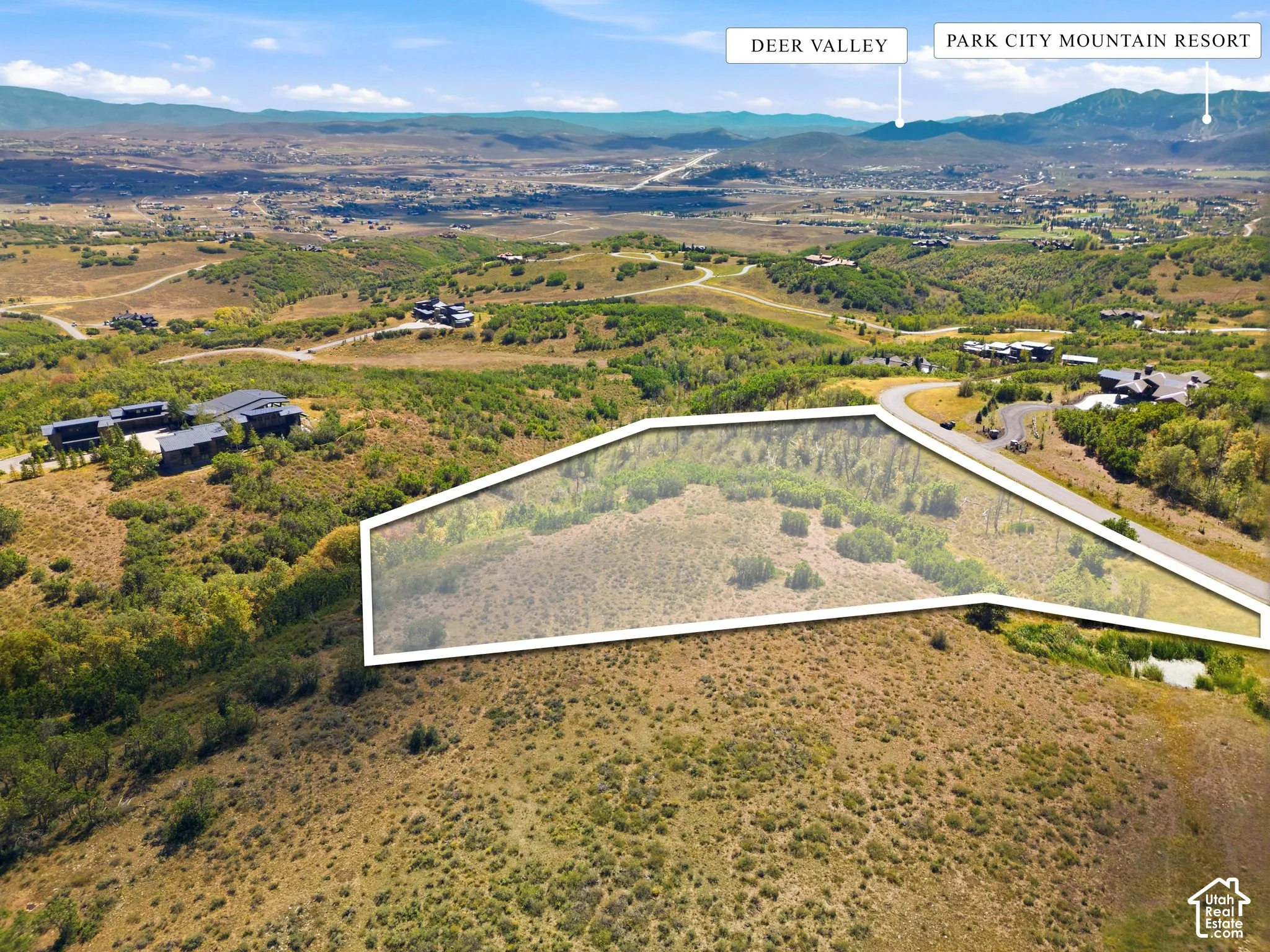 Expansive parcel of land featuring native vegetation, rolling topography, and direct access to an established paved road, characterized by panoramic mountain backdrops