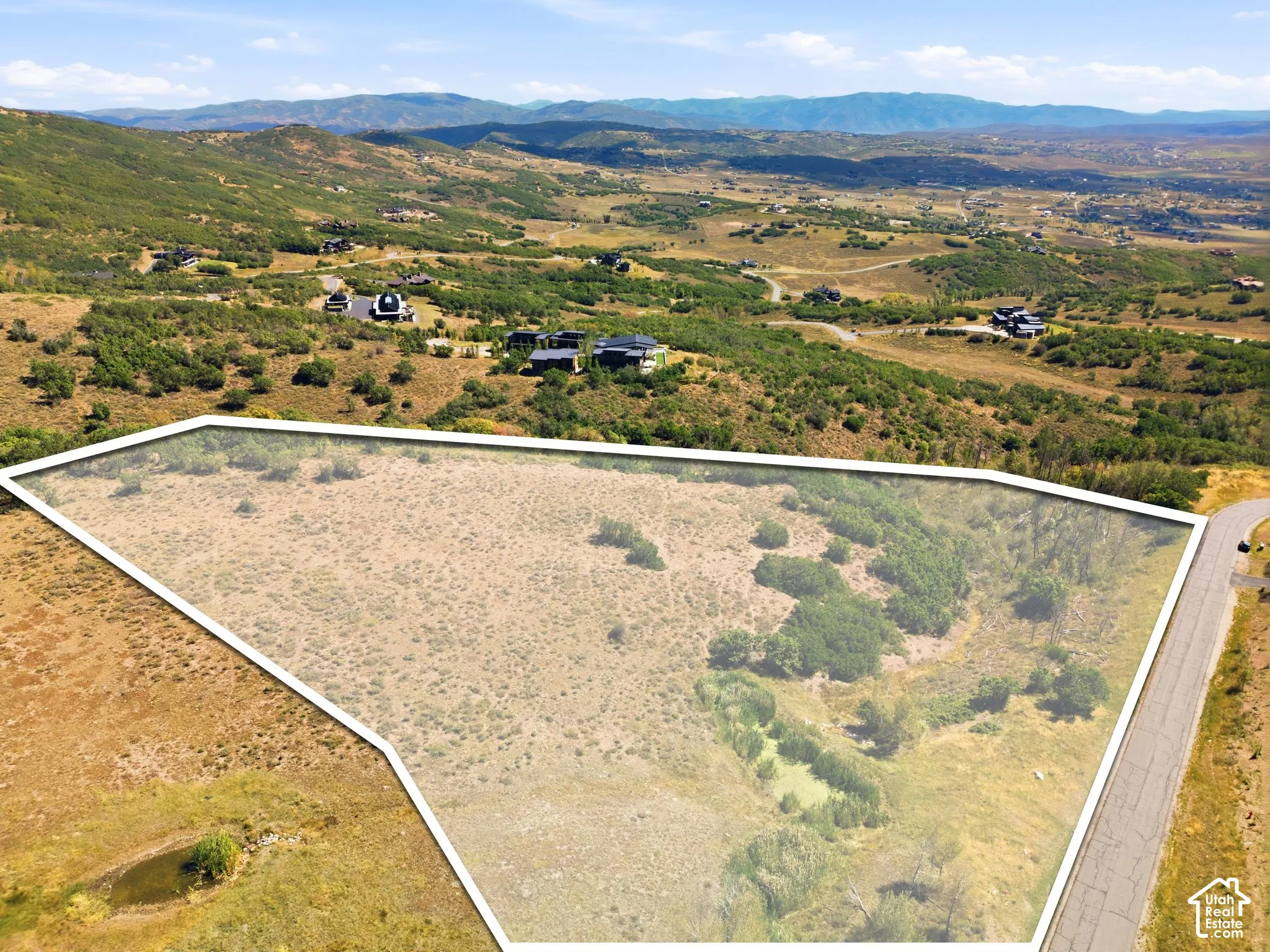 Expansive undeveloped land featuring varied terrain and natural vegetation, bordered by a paved road