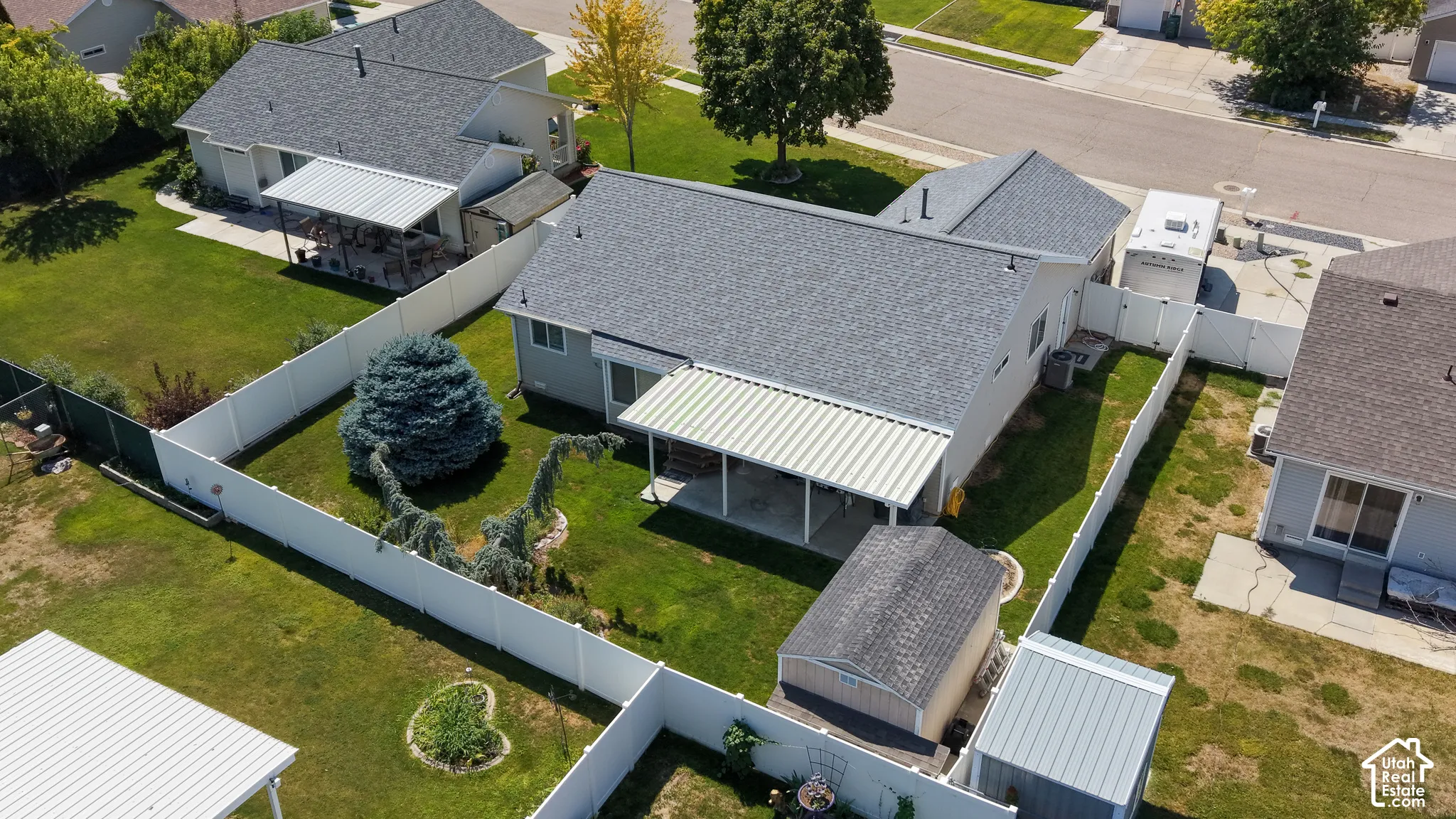 Fenced backyard featuring a covered patio, mature landscaping, and an outbuilding