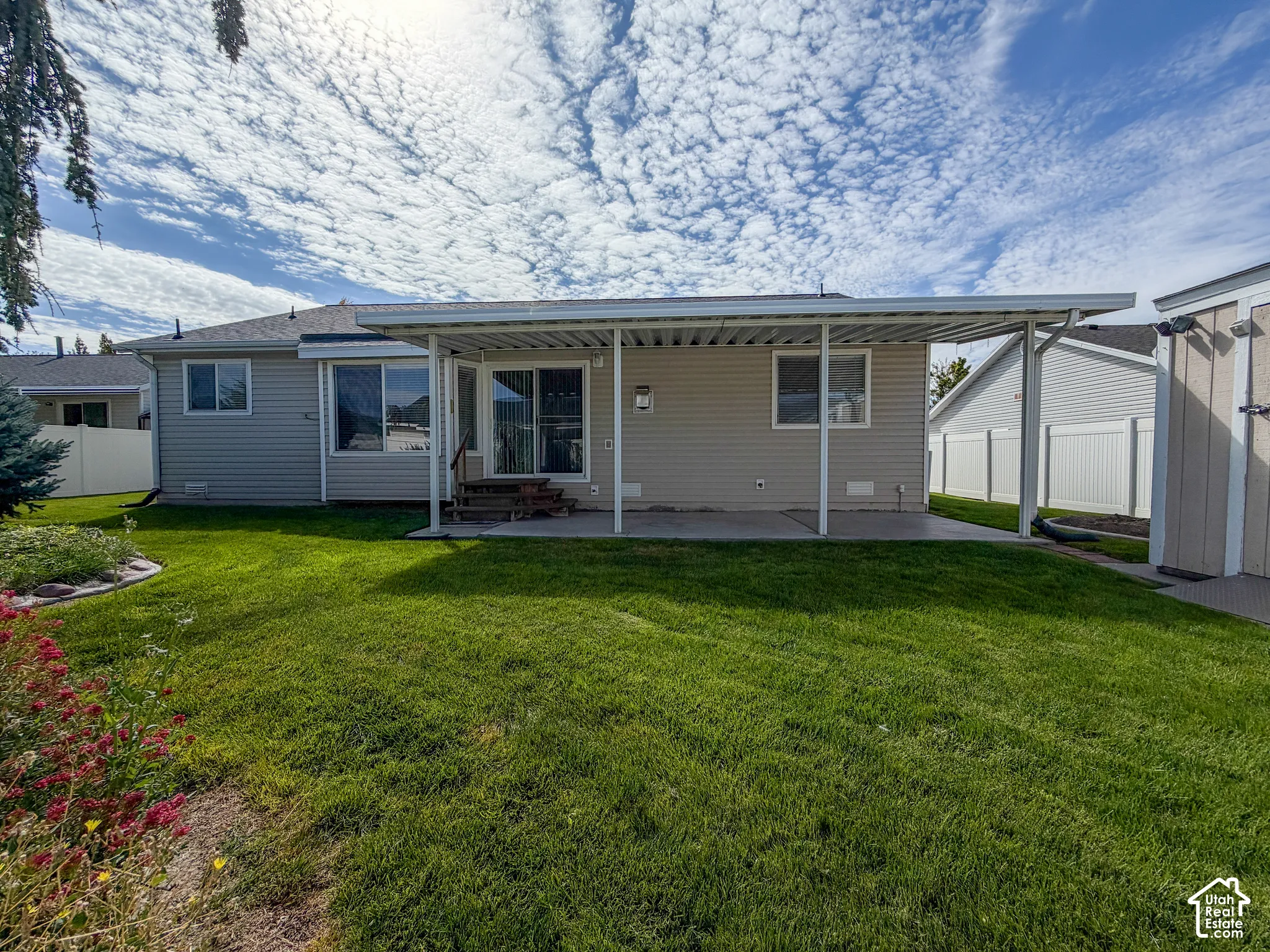 Expansive grassy yard with a covered patio, concrete surface, and sliding glass door access