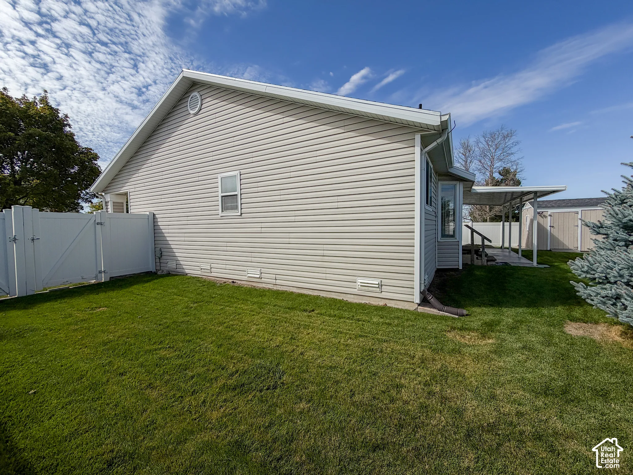 Side yard featuring a vinyl privacy fence, bay window, covered patio, and detached storage shed
