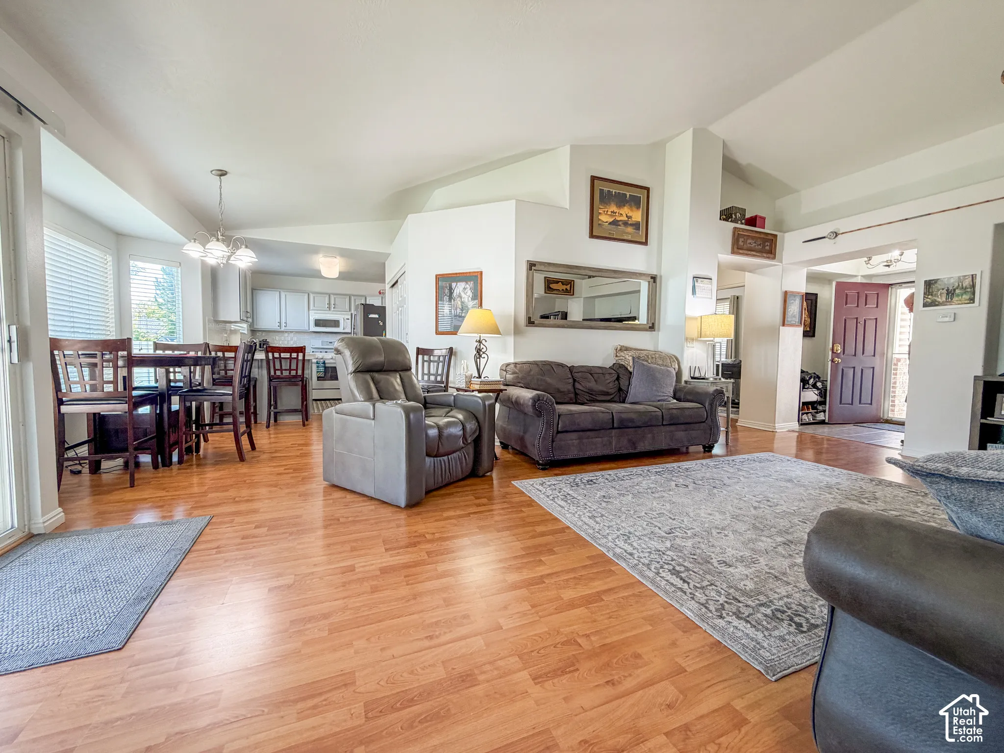 Open concept living space with wood-finish flooring, vaulted ceilings, and a dining area with a multi-light pendant