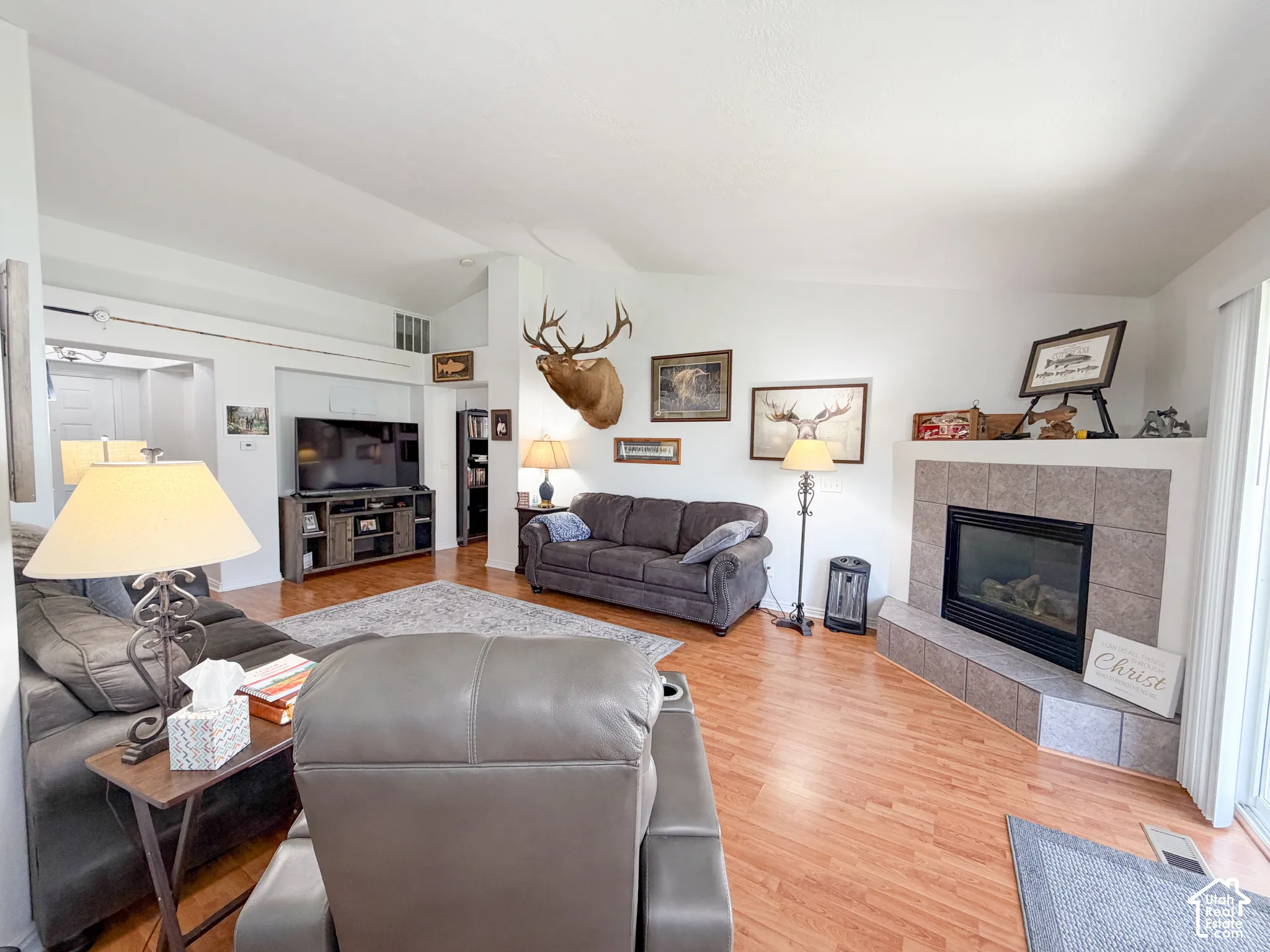 Living area featuring vaulted ceilings, wood-finish flooring, a tiled fireplace with hearth, and built-in shelving