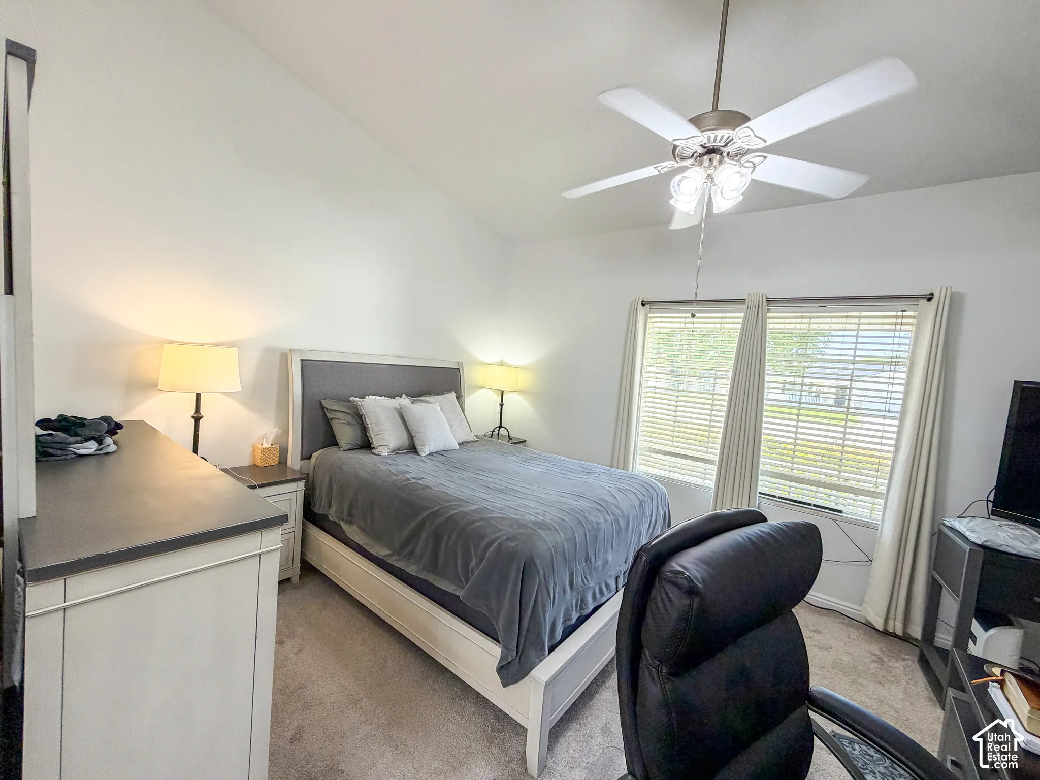 Vaulted ceiling with a ceiling fan, two windows with blinds, and carpeted flooring