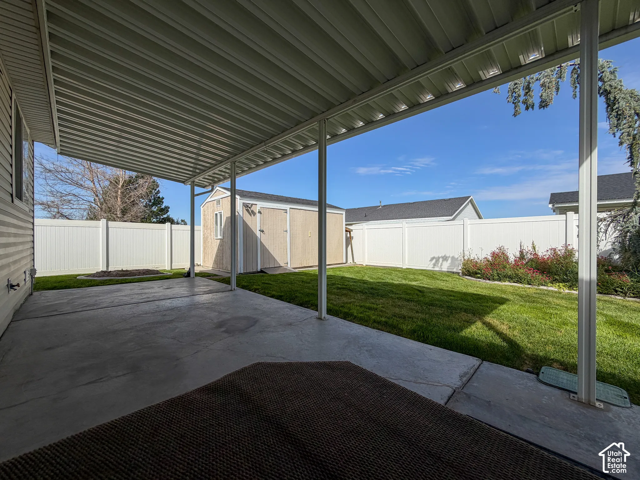Covered patio featuring concrete flooring, a manicured lawn, a detached storage shed, and a white privacy fence