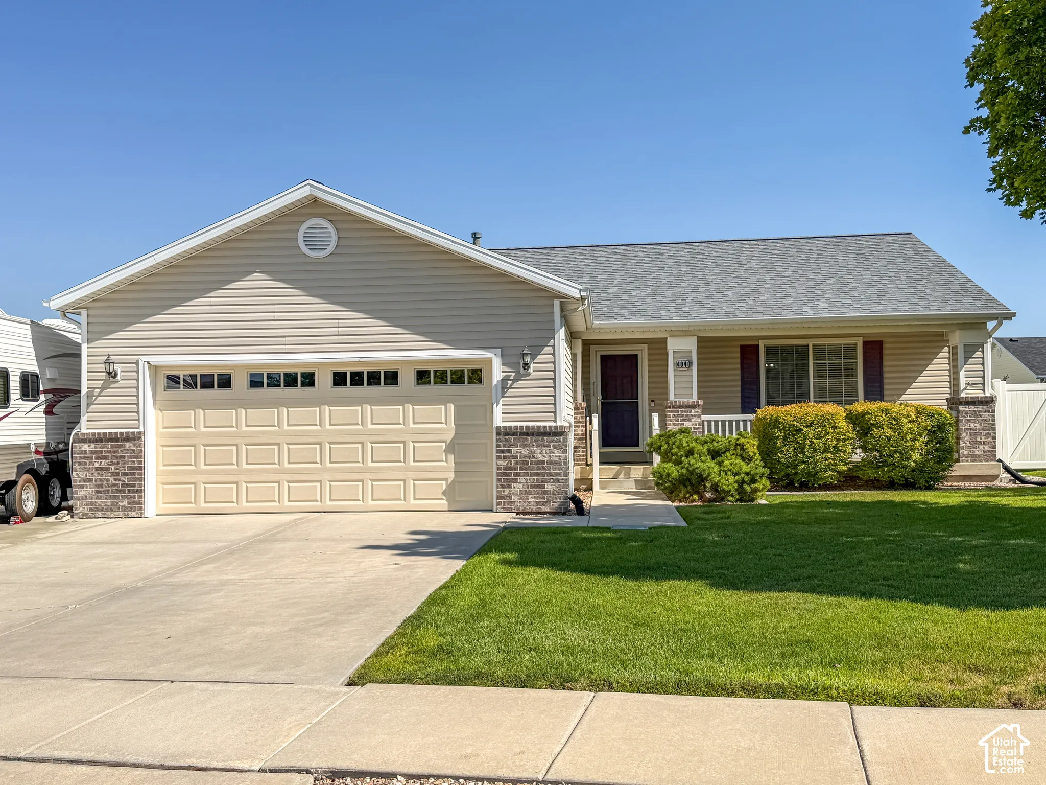 Exterior featuring beige siding, brick accents, an attached garage, a covered front porch with white railings, and a concrete driveway