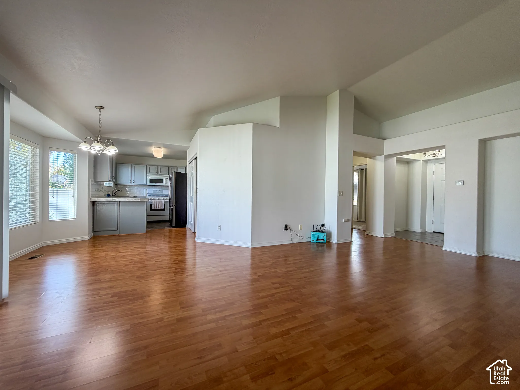 Open-concept living space with wood-finish flooring, vaulted ceilings, and a kitchen featuring grey cabinetry and white appliances