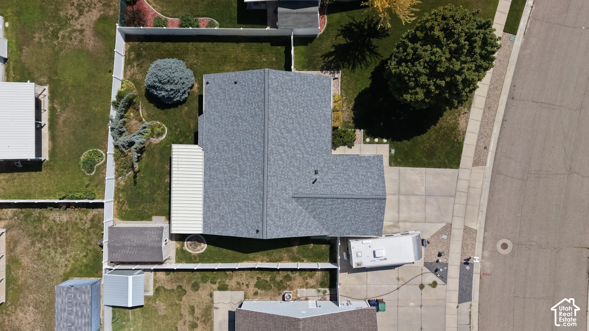 Asphalt shingle roof, paved driveway, concrete sidewalk, mature trees, and fenced backyard