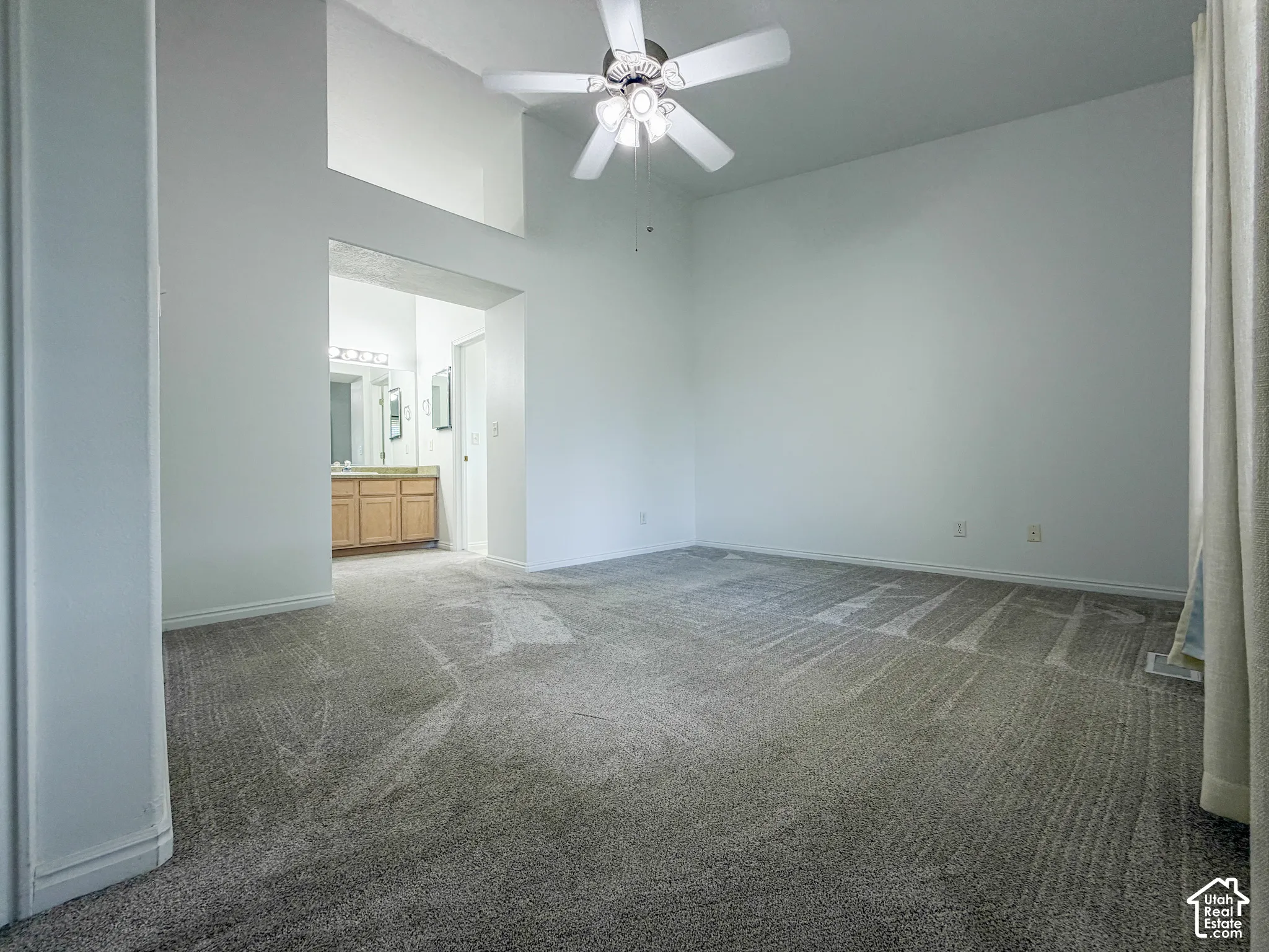 Expansive carpeted room with vaulted ceilings, a ceiling fan, and an arched entry leading to a bathroom with a wood-finish vanity