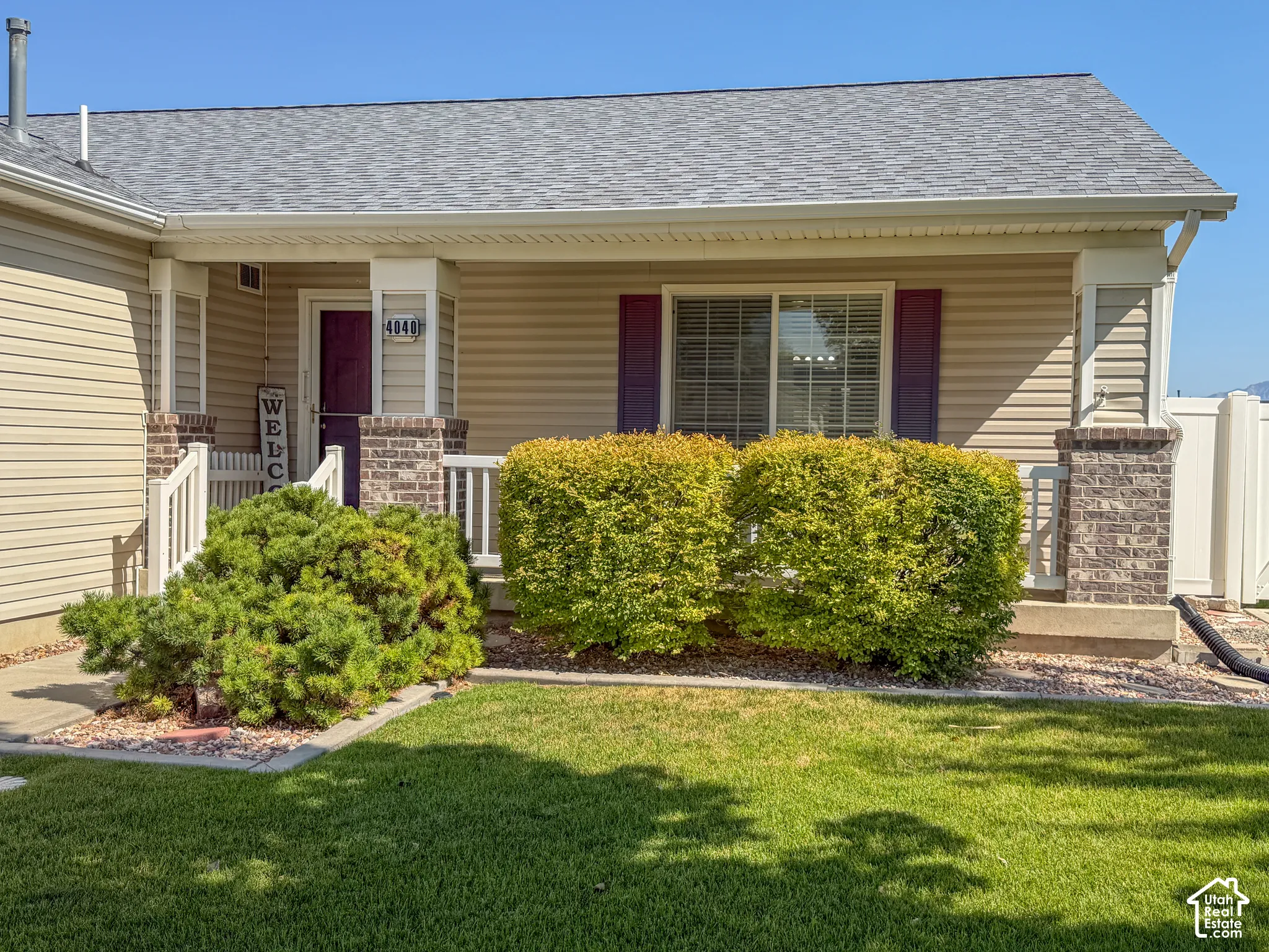 Inviting facade featuring horizontal siding, a covered porch with brick-clad columns, a dark-toned entry door, and a well-maintained lawn with established shrubbery
