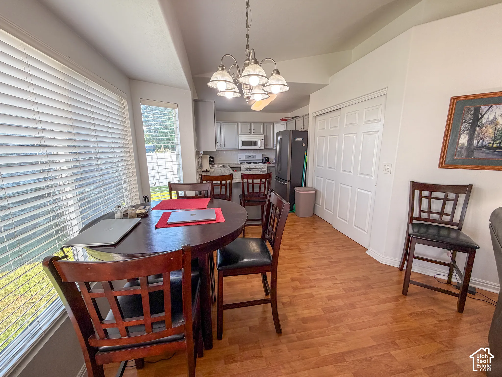 Bay window with horizontal blinds, wood-finish flooring, white bi-fold closet doors, and recessed kitchen with light-toned cabinetry
