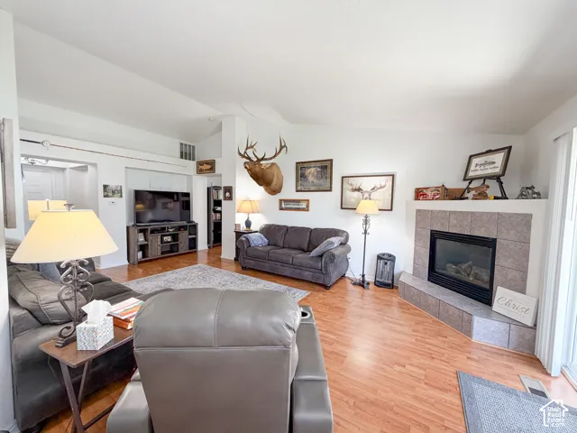 Living area featuring vaulted ceilings, wood-finish flooring, a tiled fireplace with hearth, and built-in shelving