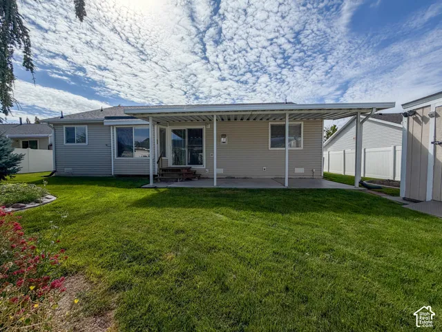 Expansive grassy yard with a covered patio, concrete surface, and sliding glass door access