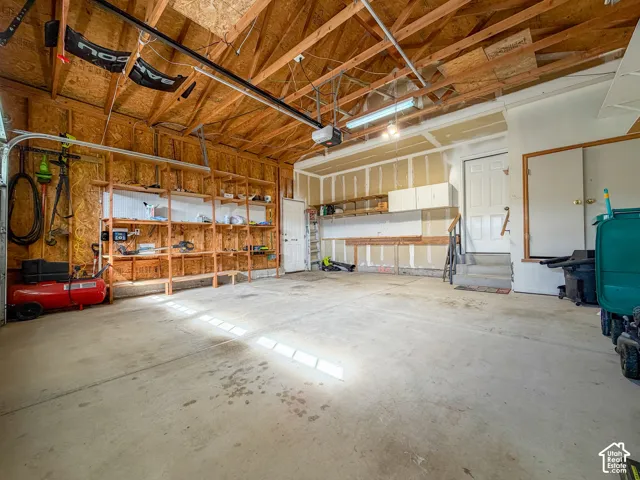 Spacious garage featuring exposed wood rafter ceiling, built-in shelving, concrete flooring, and interior access door